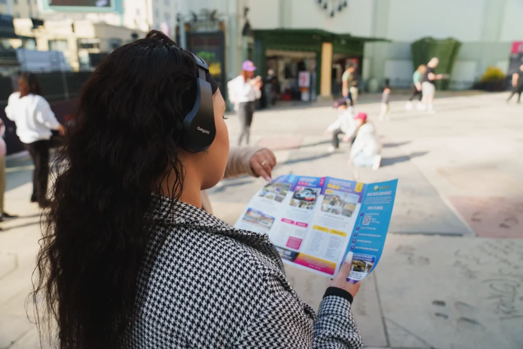 Person wearing headphones holding a Hollywood Bus Tours map on Hollywood Boulevard.