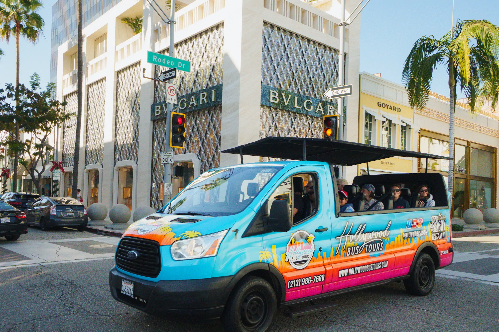 Hollywood Bus Tours open air bus driving past luxury stores on Rodeo Drive in Beverly Hills with passengers onboard