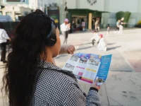 Person wearing headphones holding a Hollywood Bus Tours map on Hollywood Boulevard.