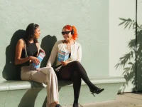 Two tour guests sitting and chatting while holding Hollywood Bus Tours brochures in Los Angeles.